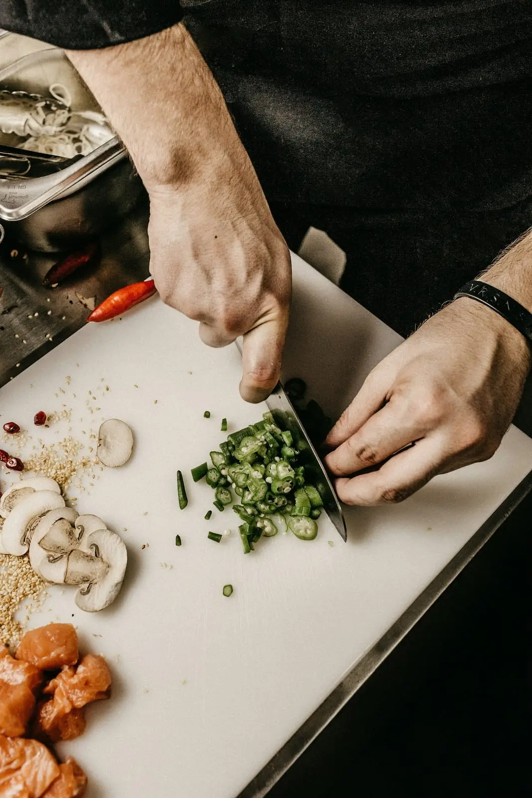 Mains d'un cuisinier émincant des légumes sur une planche