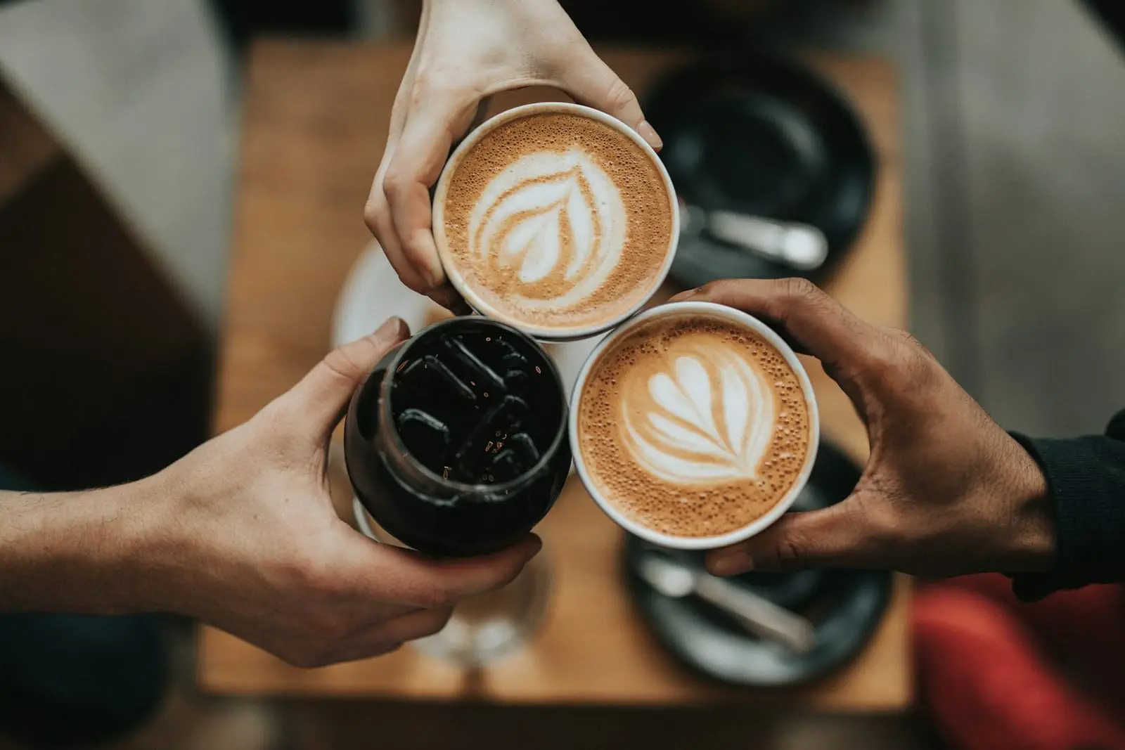 Trois mains trinquent avec des cafés au-dessus d'une table