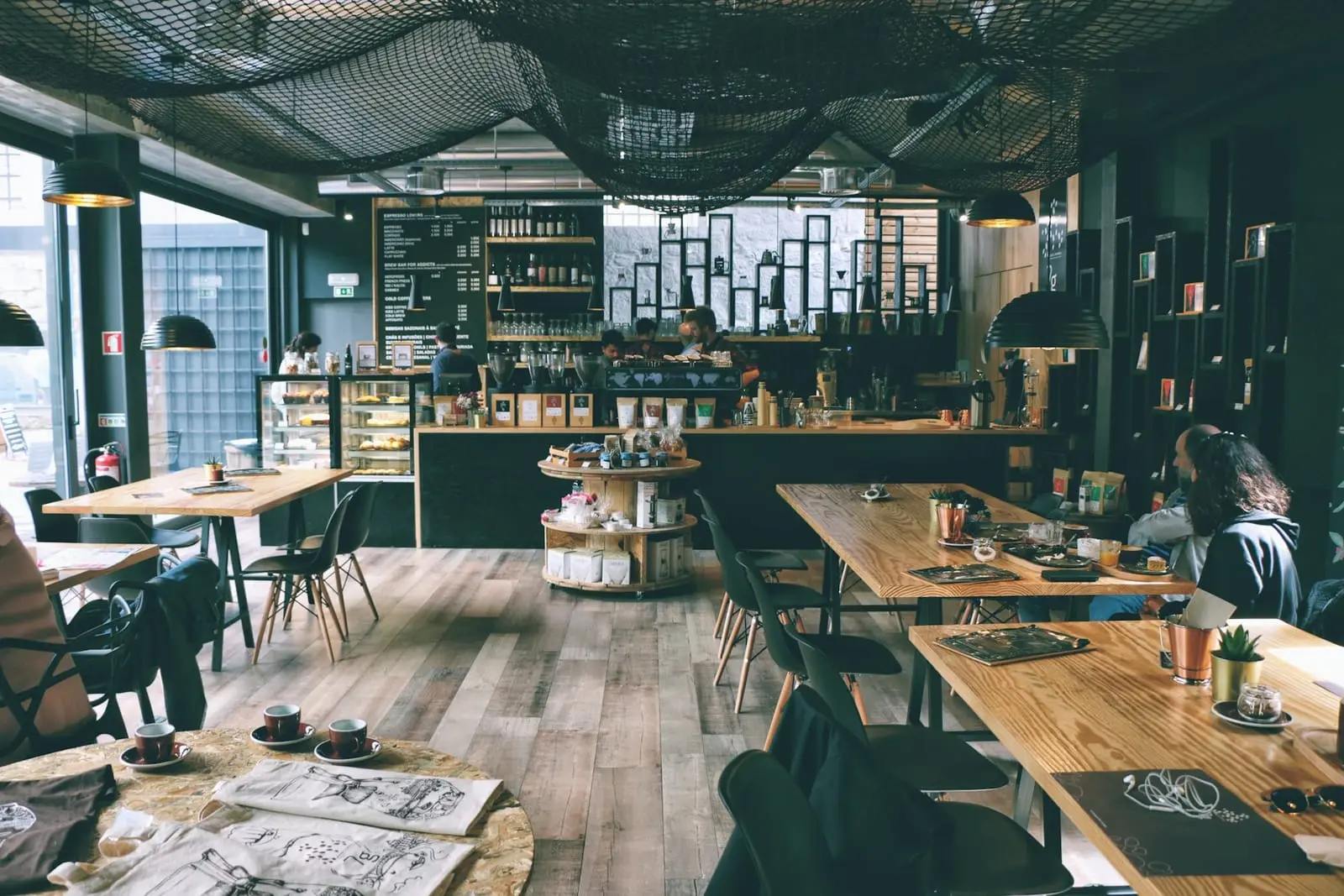 Salle du café avec parquet, tables en bois et grandes baies