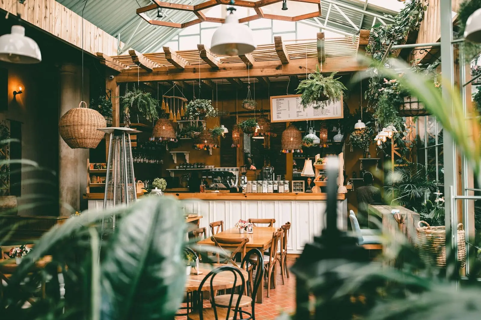 Salle lumineuse sous verrière, plantes suspendues et tables en bois